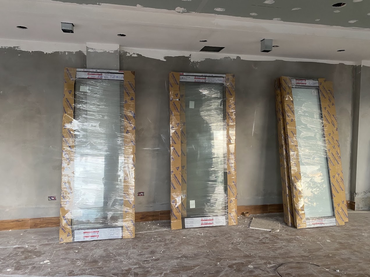 Ba tấm cửa kính khung nhôm mới bọc nilon dựng trong phòng đang thi công